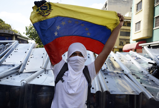 A demonstrator holds a Venezuelan flag in front of riot policemen &#8211; en