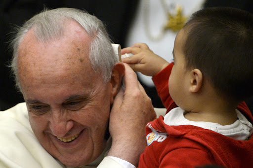 A child plays with Pope Francis&#8217; skull cap during an audience with beneficiaries and volunteers of the Santa Marta pediatric dispensary &#8211; en