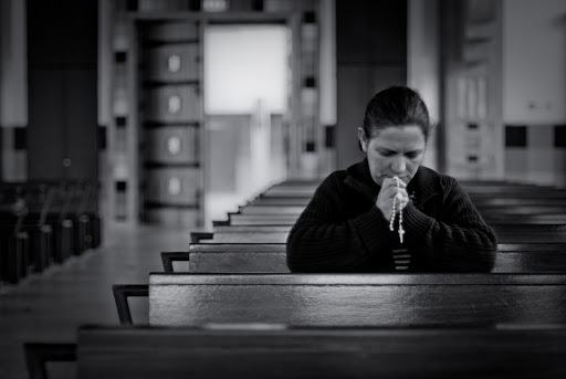 Woman praying rosary alone in church
