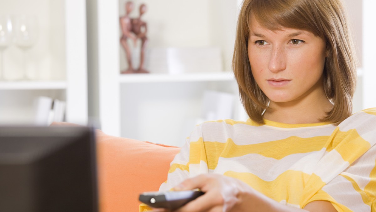 WEB3 YOUNG WOMAN WATCHING TV TELEVISION YELLOW SERIOUS Shutterstock