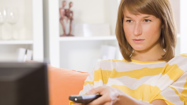WEB3 YOUNG WOMAN WATCHING TV TELEVISION YELLOW SERIOUS Shutterstock