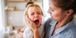 A mother holding a crying toddler daughter indoors in kitchen