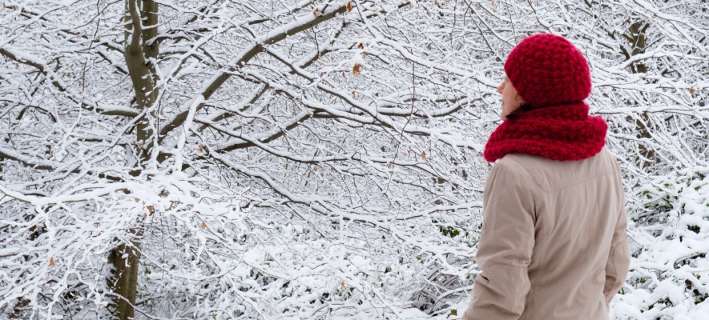 Woman in red knit cap standing in snowy forest side view