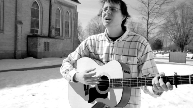 Jacob Rudd plays guitar near church, black and white