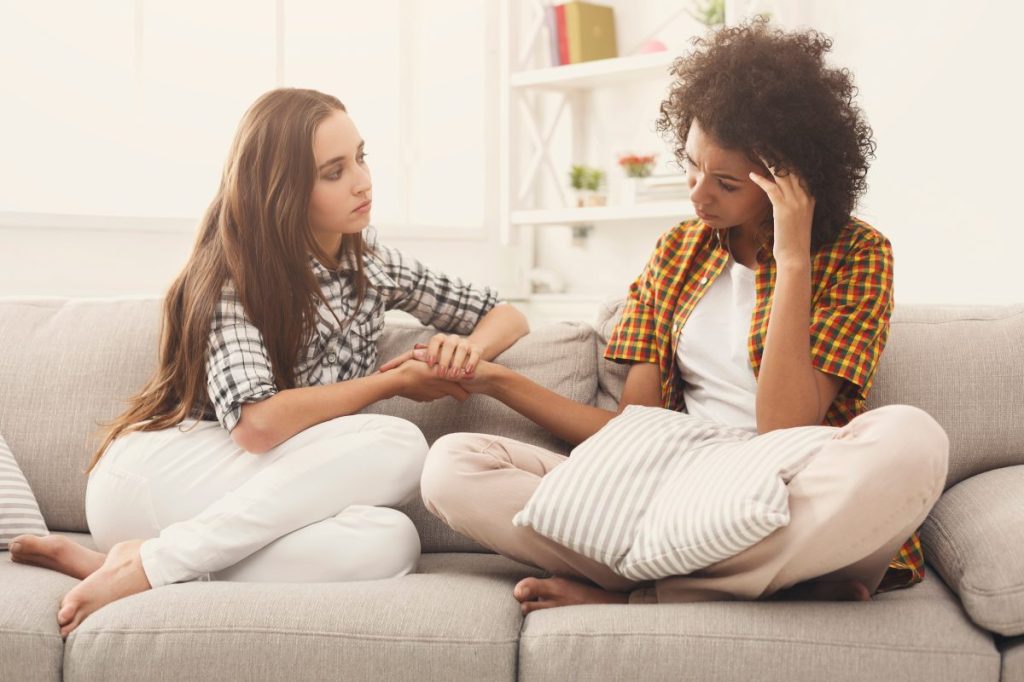 Two women sitting on a couch, one consoling the other