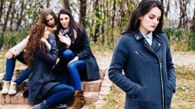 Sad-girl-with-friends-gossiping-in-background-behind-her-back-shutterstock