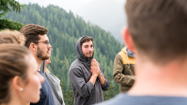 young group of men and women stand in a circle and prepare to have a group prayer outdoors