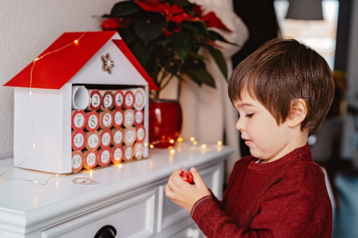 Little child taking chocolate opening first day in handmade advent calendar made from toilet paper rolls. Sustainable Christmas, kids seasonal activities