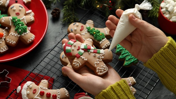 Making homemade Christmas cookies Girl decorating gingerbread man at black table closeup
