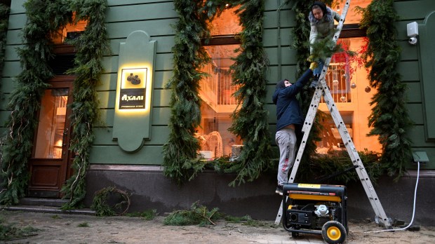 Employees decorate a window of a cafe which electricity comes from a power generator standing outside - Ukraine