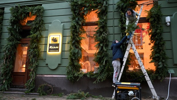 Employees decorate a window of a cafe which electricity comes from a power generator standing outside - Ukraine