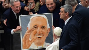 A visitor holds a portrait of Pope Francis as he passes