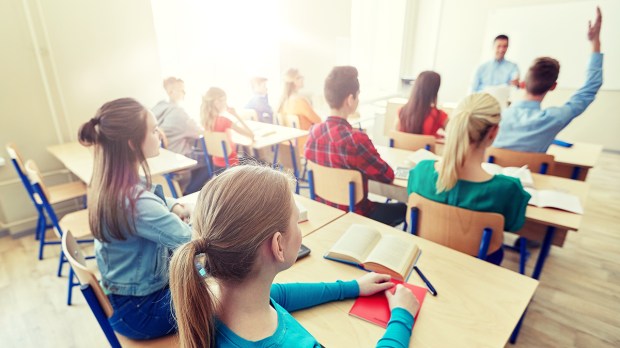 group-of-happy-students-raising-hands-and-teacher-in-classroom