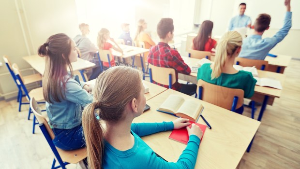 group-of-happy-students-raising-hands-and-teacher-in-classroom