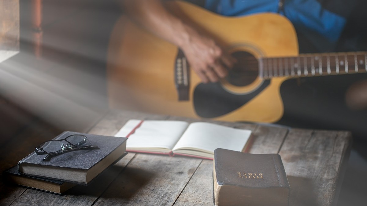 Man plays guitar with bible and open notebook.