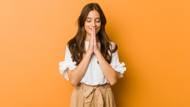 uśmiechnięta młoda dziewczyna modli się ze złożonymi rękami