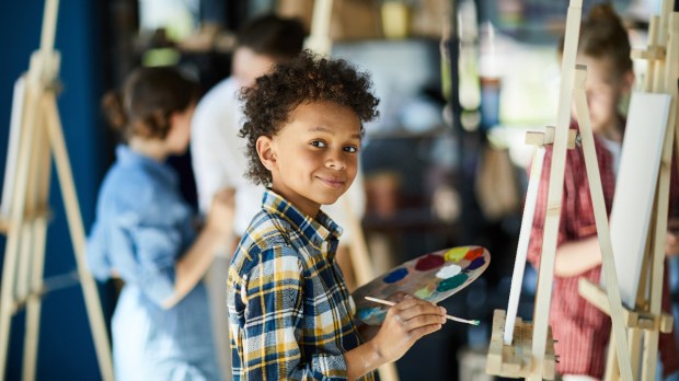 Young boy with color palette standing by easel painting
