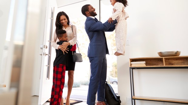 Children Greeting And Hugging Working Parents As They Return Home From Work