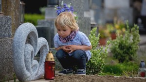 Little-toddler-boy-sitting-on-a-grave-in-cemetery-sad-and-lonely-shutterstock