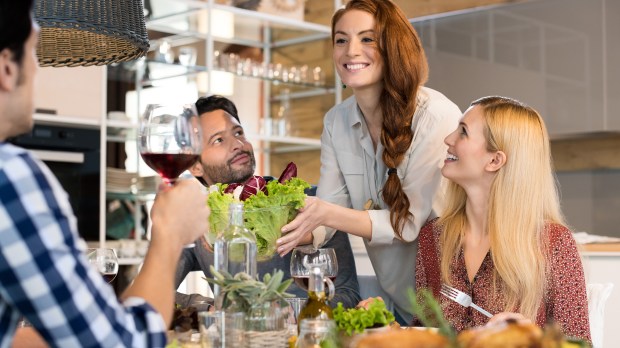 Smiling woman serving salads to her friends at home