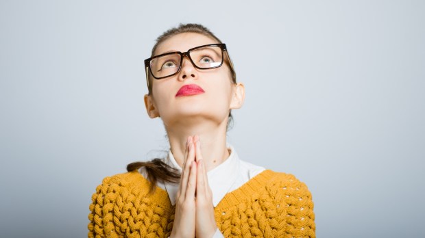 Kobieta w okularach modli się ze złożonymi rękami i patrzy w górę wyczekując spełnienia prośby