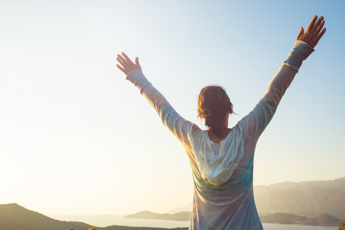 Happy traveler, woman with open arms stands on the rock