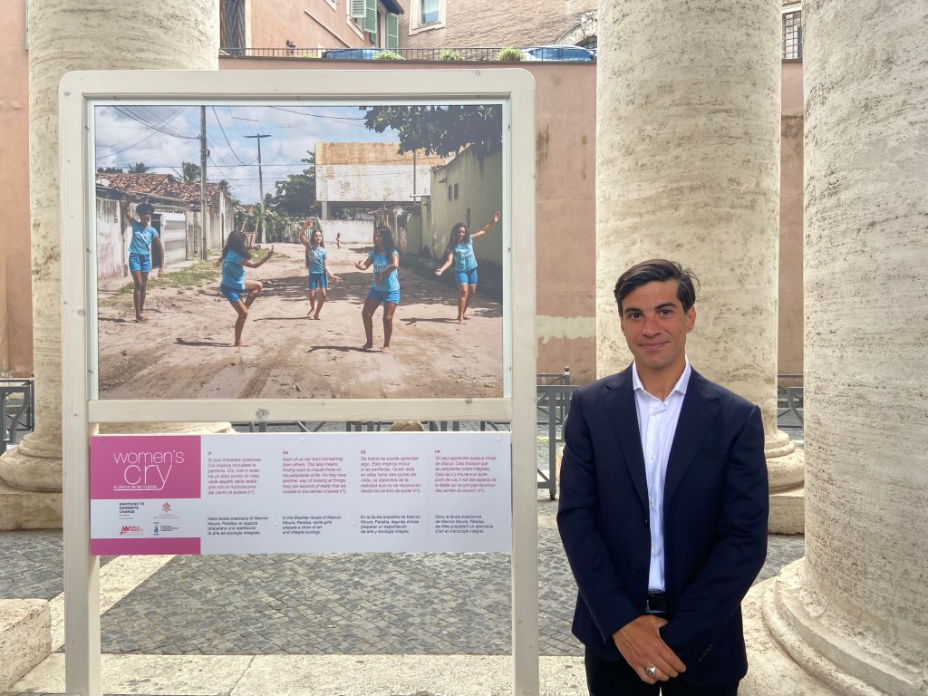 One of the photographers, Sebastiano Rossitto, whose work is featured in the "Women's Cry" exhibit poses next to his photo showing a group of girls dancing in a slum in Brazil