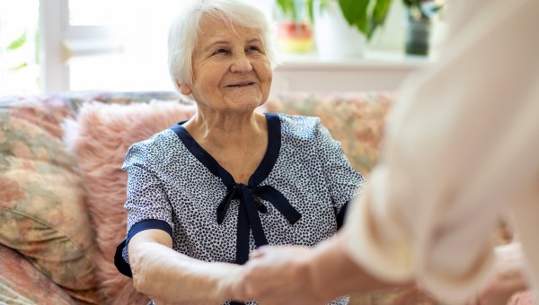 An elderly woman smiling at a person holding their hands