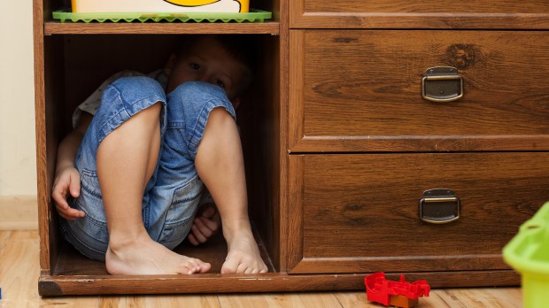 child hiding feet cabinet