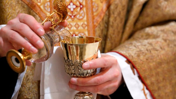 Ksiądz podczas Mszy nalewa wodę do kielicha z winem