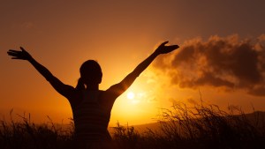 woman with hands raised toward sunrise