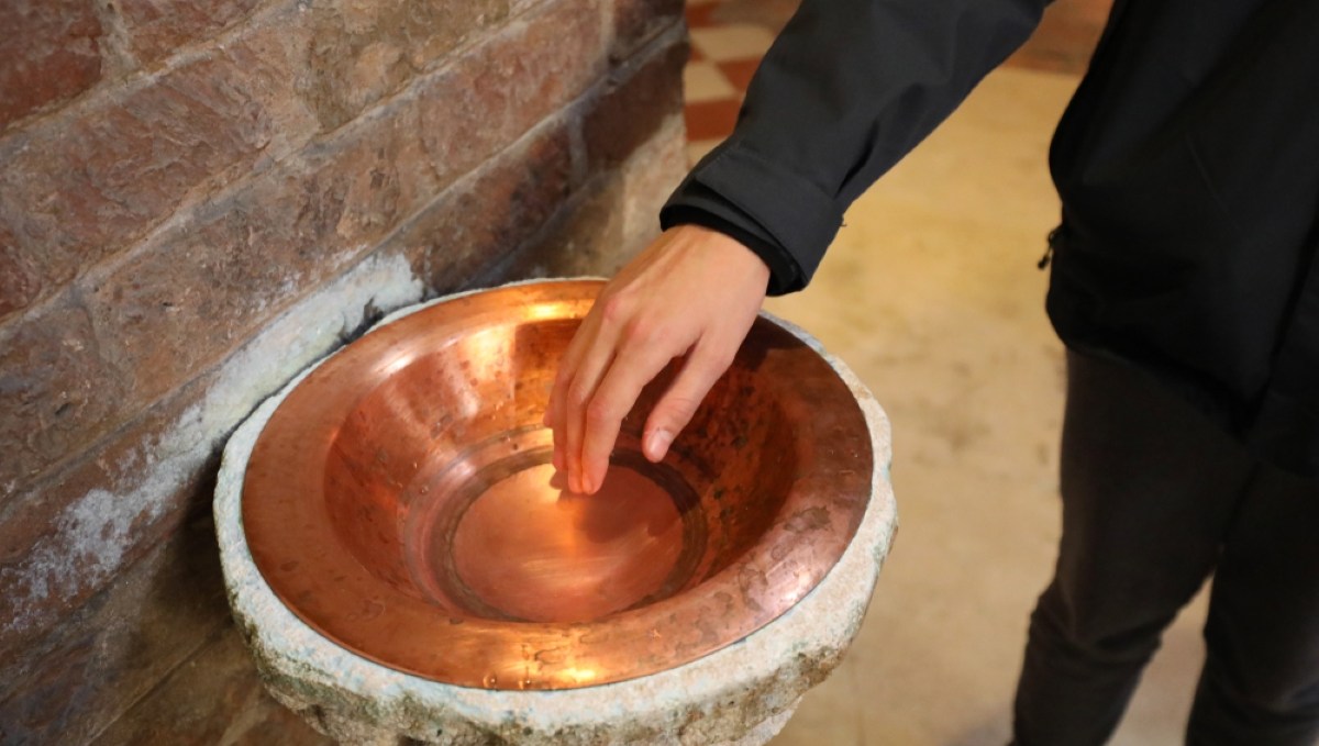Faithful plunges his hand into the holy water of a Catholic church to make the sign of the cross