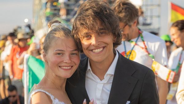 A Polish couple wearing a wedding dress and a suit smile at the camera at World Youth Day 2023 in Lisbon