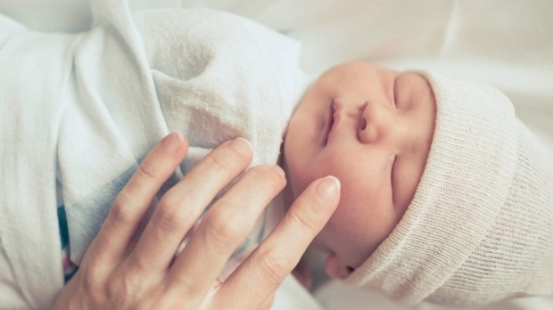 Swaddled baby with mother's hand touching face