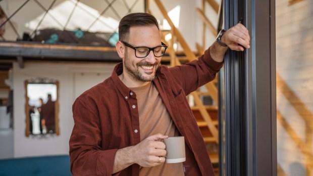 Wdzięczny i radosny mężczyzna stoi z kubkiem kawy w nowoczesnym wnętrzu