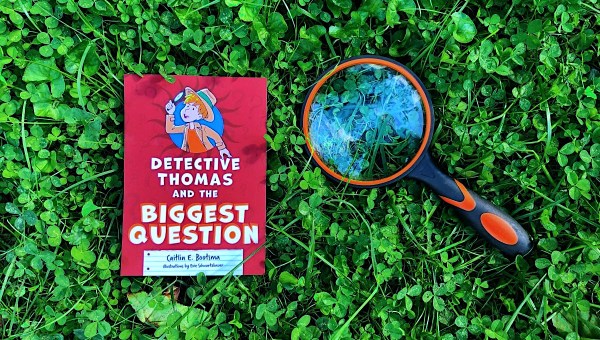 Kids book "Detective Thomas and the Really Big Question" on lawn with magnifying glass