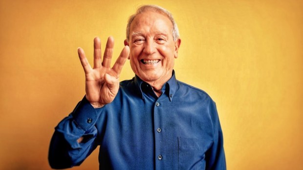An elderly man holds up four fingers