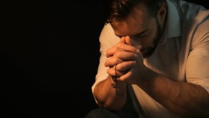 Religious young man praying to God on black background
