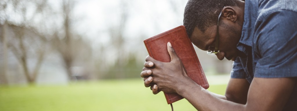 A young African-American male sitting with closed eyes with the Bible in his hands