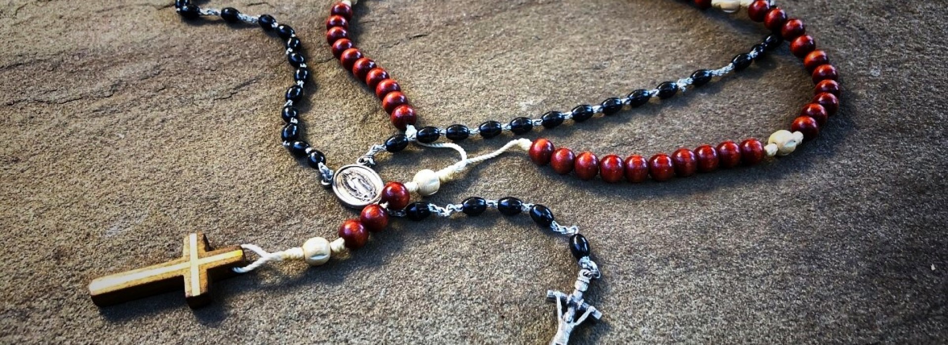 Two entwined rosaries, one black and one brownish red, placed on a slab of granite.