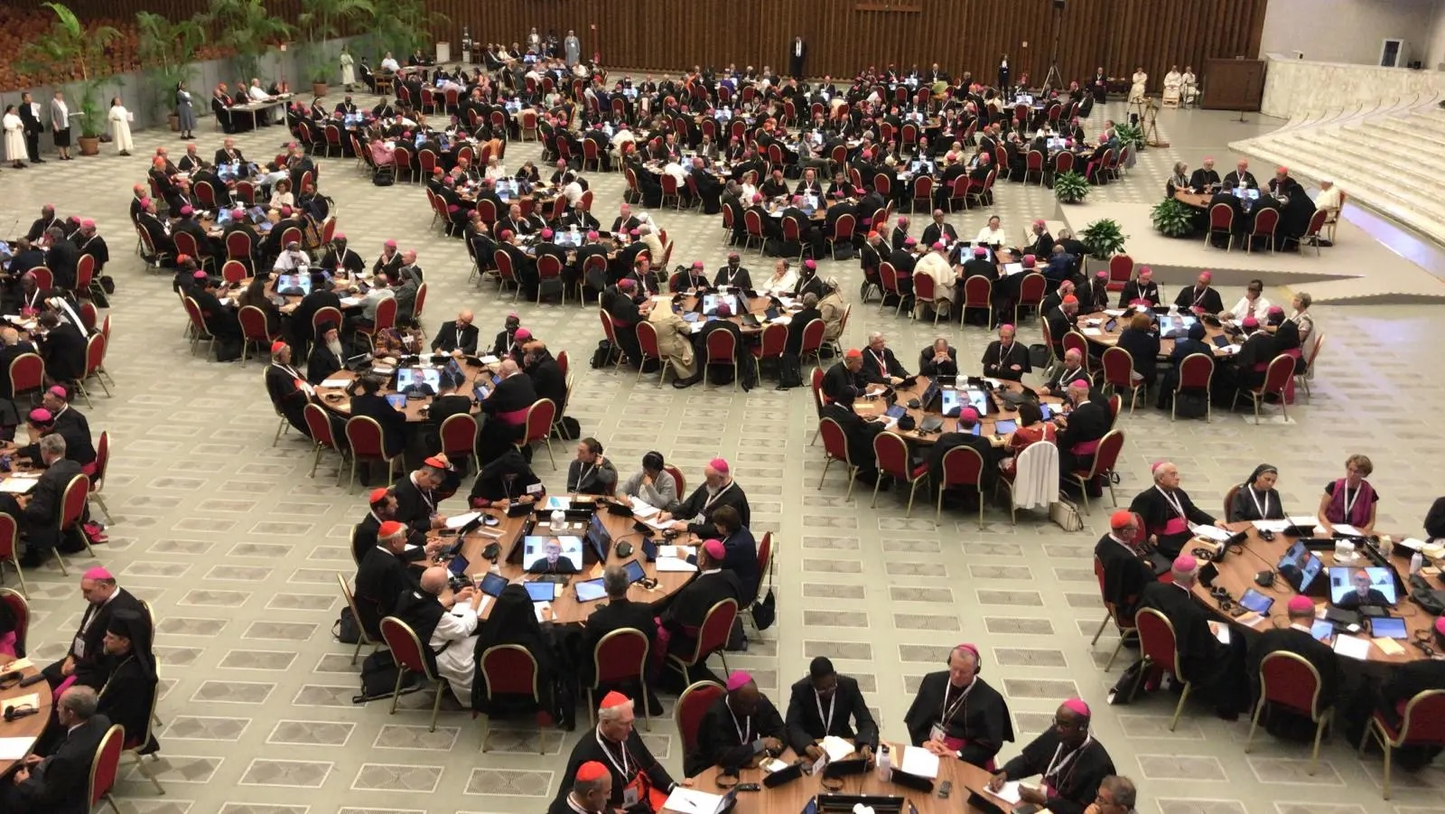 Synod members sitting at tables in Paul VI Hall during the Synod on Synodality