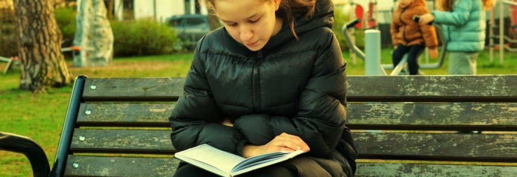 Girl reading a book on a park bench in the autumn wearing down jacket