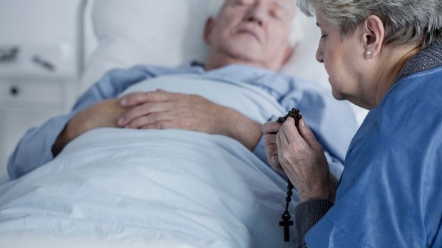 woman praying over man in sickbed