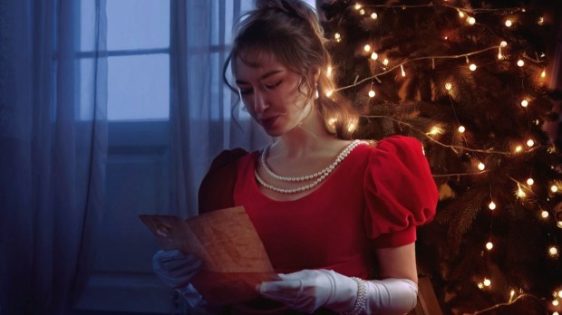 Young girl from 19th century in a red dress reading a letter with the background of a Christmas tree