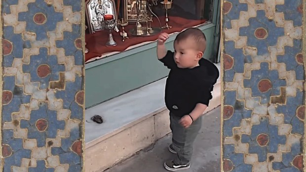 Little boy making sign of the cross in front of religious shop