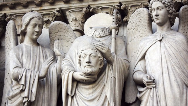 Sculpture of Saint Denis carrying his head on western facade of the catholic cathedral Notre Dame de Paris