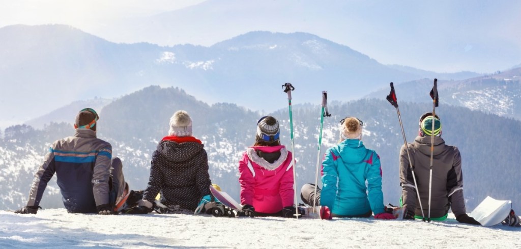 Group of friends sitting on mountain in skiing attire