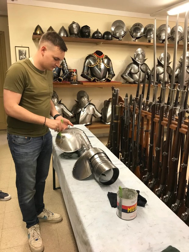 A Swiss Guard brushes a recruit's cuirass with oil.