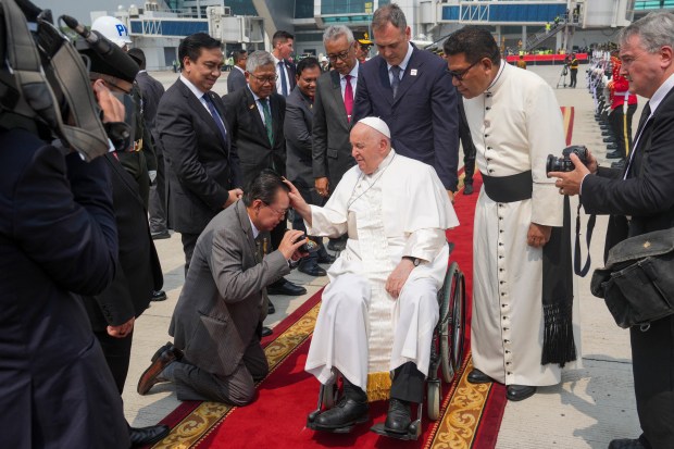 A man kneels before Pope Francis (C) upon his arrival for a farewell at Jakarta's Soekarno-Hatta International Airport ahead of his departure to Papua New Guinea's capital Port Moresby on September 6, 2024.