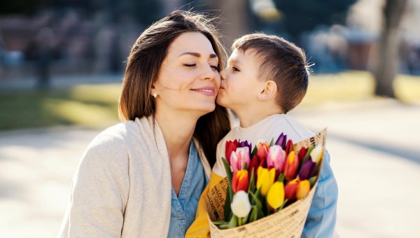 A little boy giving bouquet of tulips to his mother and kissing her on mother's day